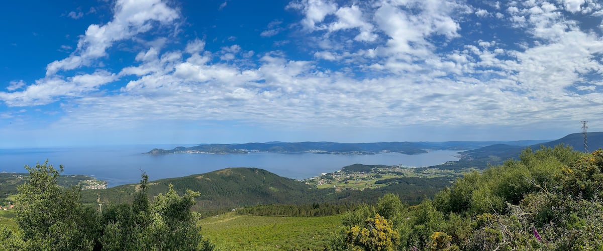A coastal landscape with rolling hills, a clear blue sky, and a view of the sea.