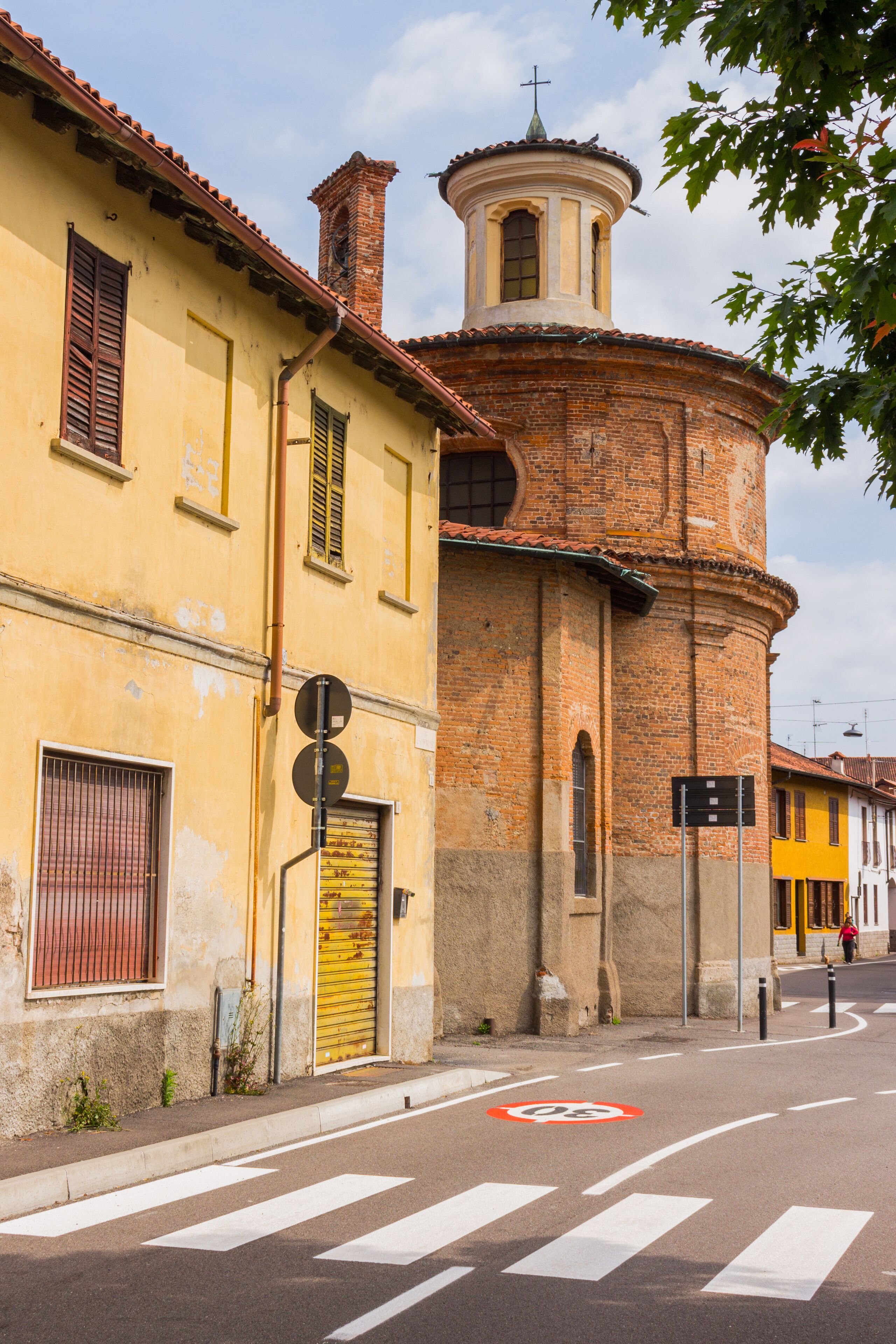A street with a yellow building, a brick tower, and a cross on top.