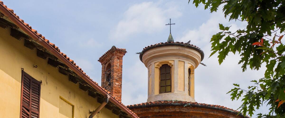 A street with a yellow building, a brick tower, and a cross on top.