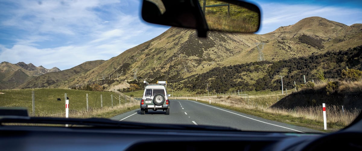 A car driving on a road with a mountain in the background.