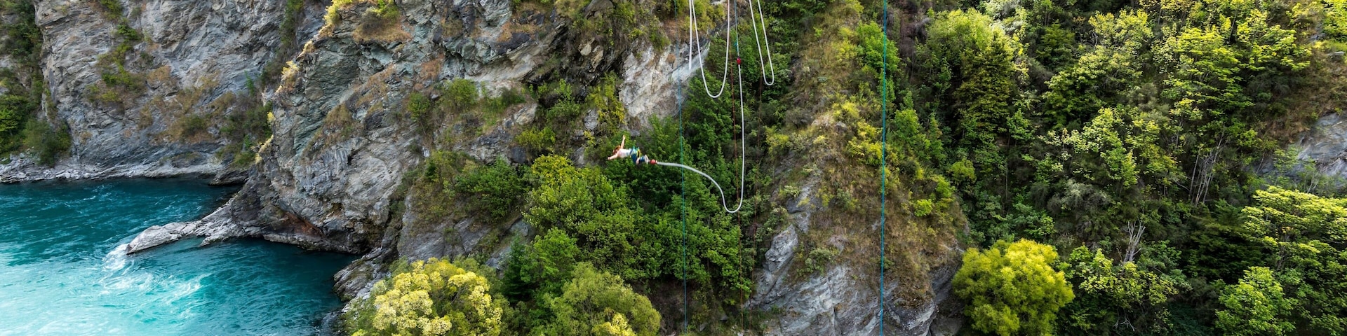 Uma ponte vermelha sobre um rio turquesa, com penhascos rochosos e vegetação verde.
