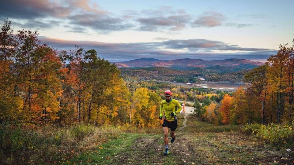 A runner on a trail surrounded by autumn foliage and distant mountains.