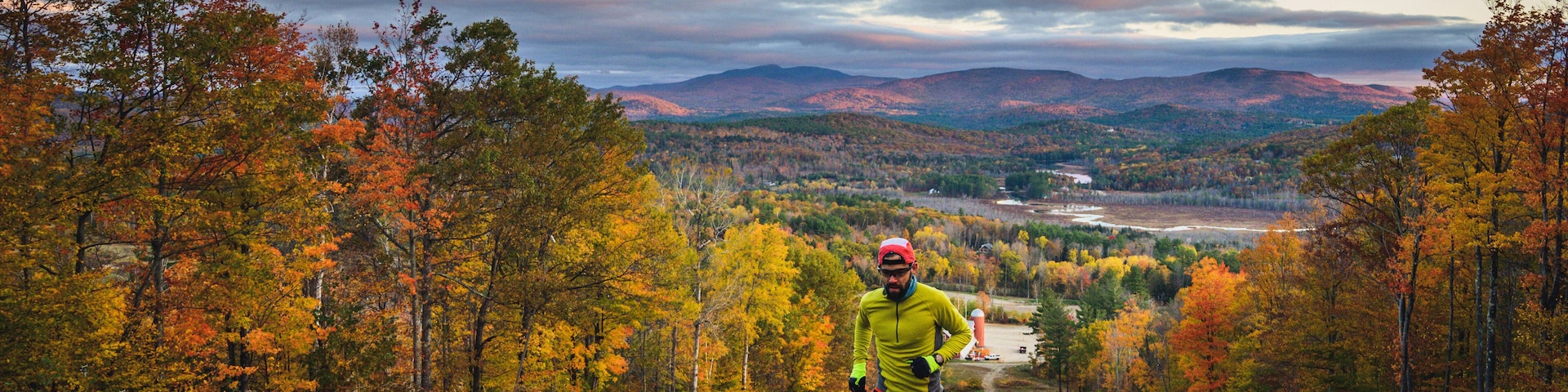 A runner on a trail surrounded by autumn foliage and distant mountains.