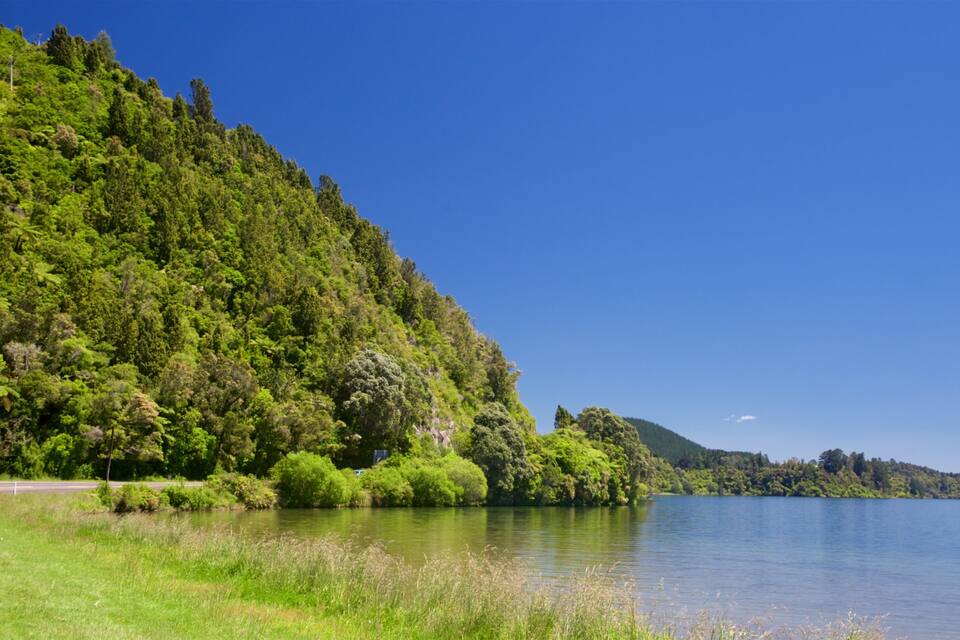 A calm lake surrounded by lush green hills and a clear blue sky.