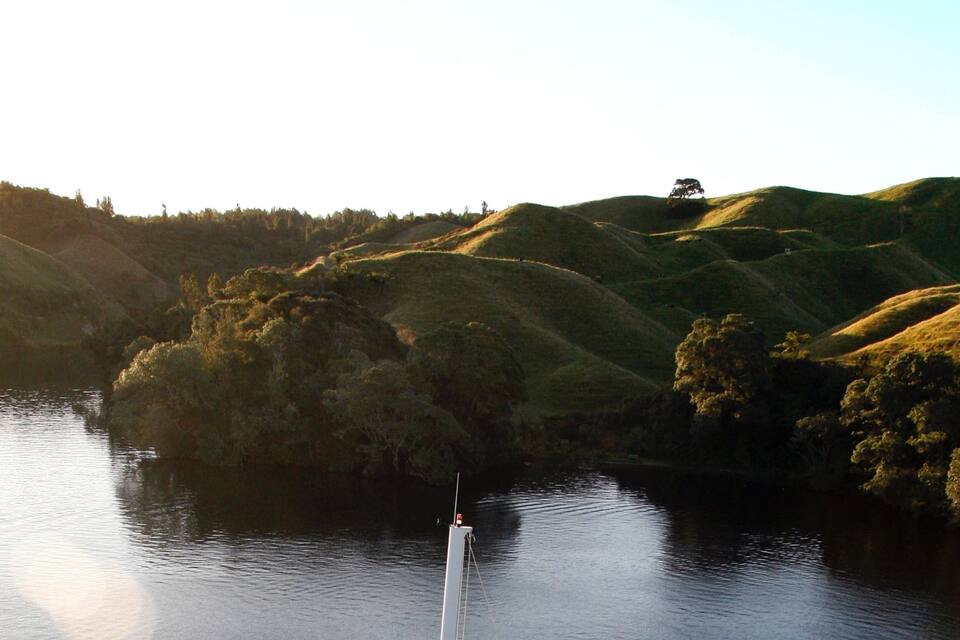 A boat on a calm river surrounded by rolling hills and dense trees.