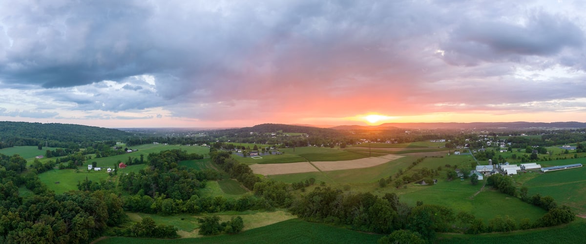 A rural landscape with fields, a small town, and a sunset.