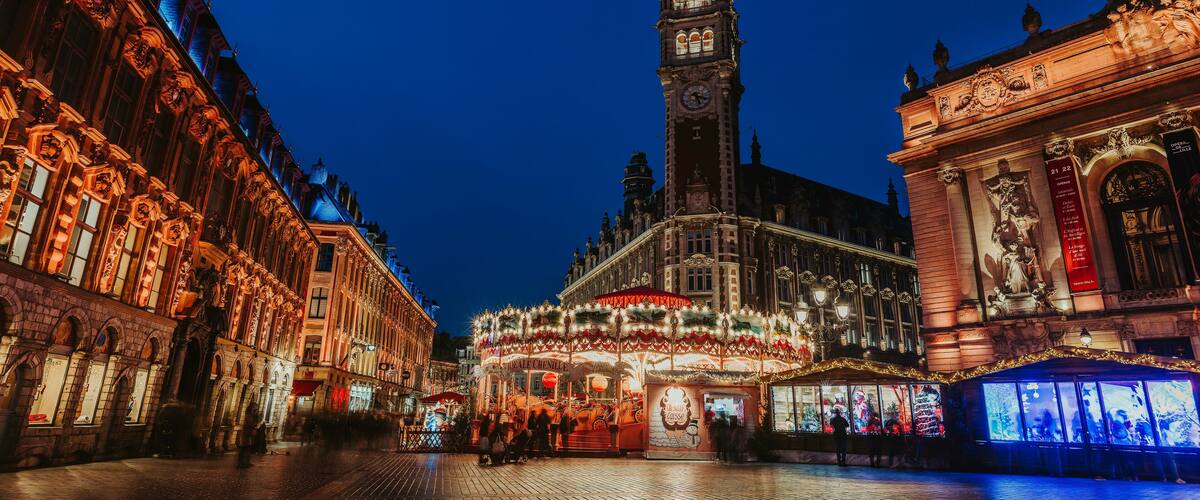 A historic square with ornate buildings, a prominent clock tower, and a festive carousel.