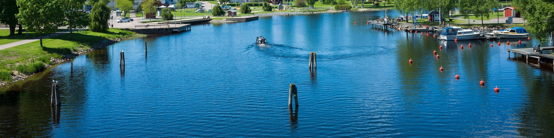 Um lago tranquilo com barcos, cais e casas ao fundo.