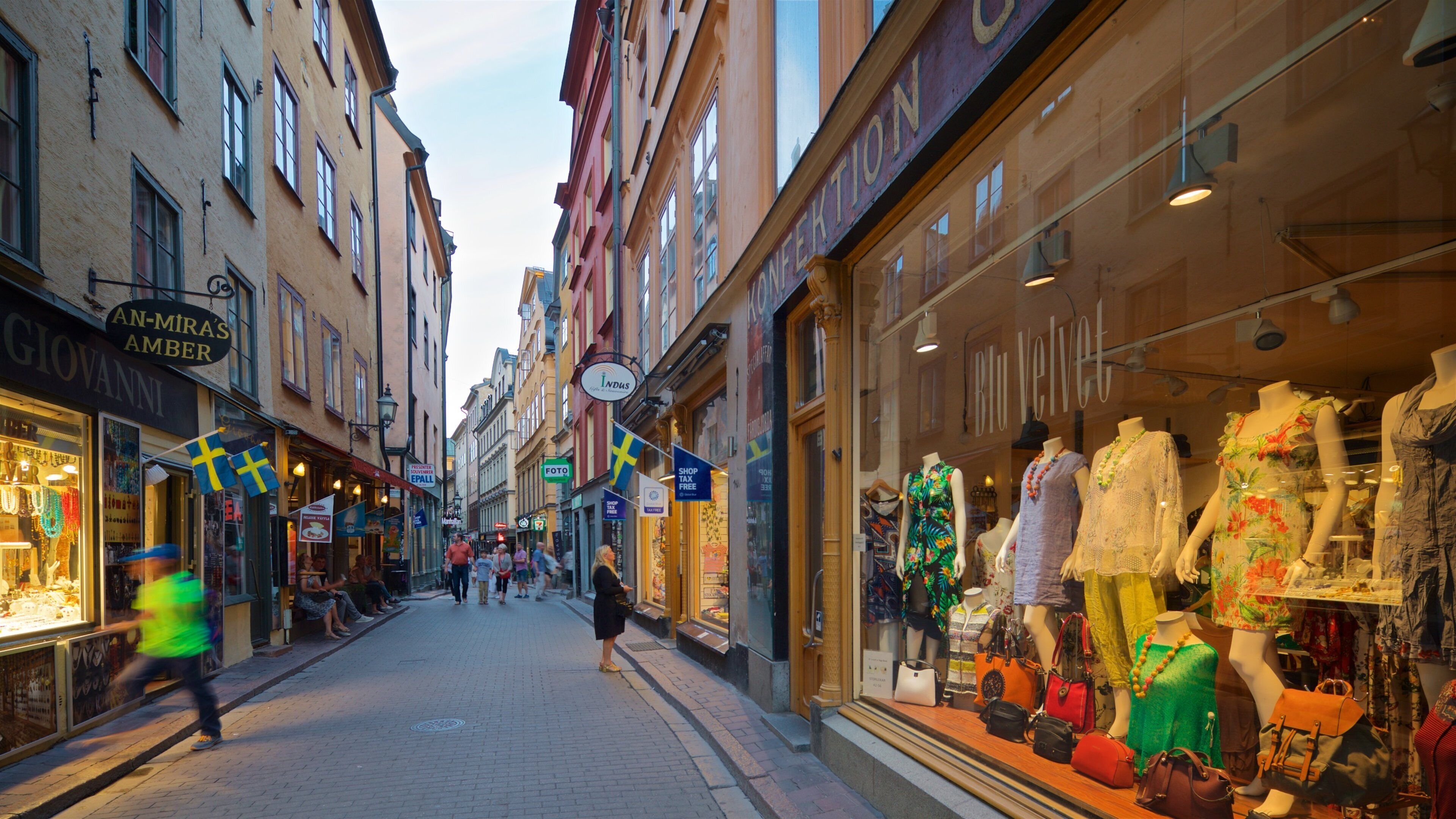 A street with shops, mannequins displaying clothes, and Swedish flags.