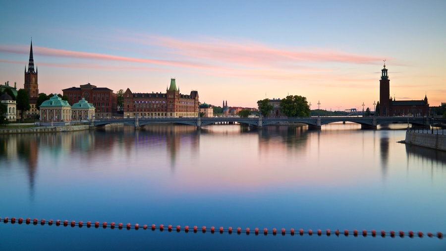 Ein Fluss mit einer Brücke, historischen Gebäuden und einem Turm, der sich im Wasser spiegelt.
