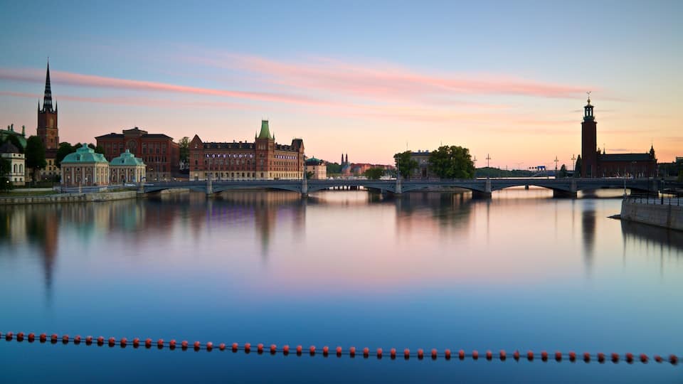 Ein Fluss mit einer Brücke, historischen Gebäuden und einem Turm, der sich im Wasser spiegelt.