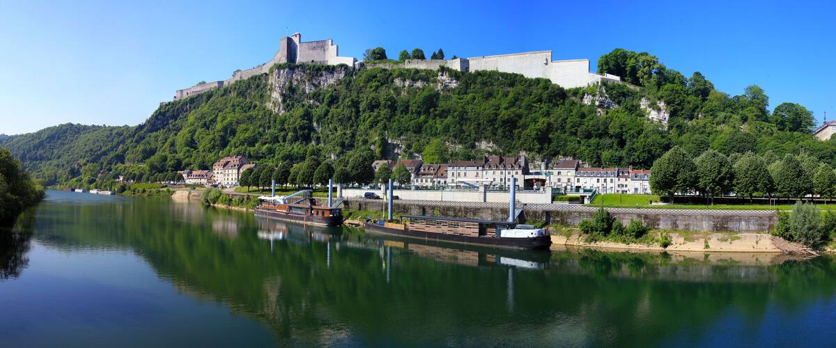 A river with a boat, a castle on a hill, and buildings along the riverbank.