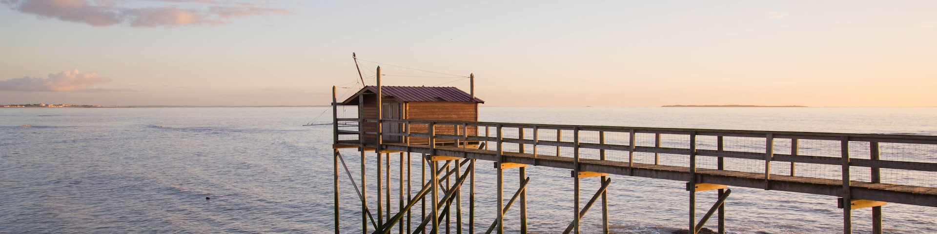 Un muelle de madera se extiende sobre aguas tranquilas, con una pequeña construcción de madera al final, y una costa rocosa.