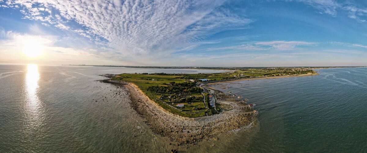 An aerial view of a coastal island with a lighthouse, a beach, and a small settlement.
