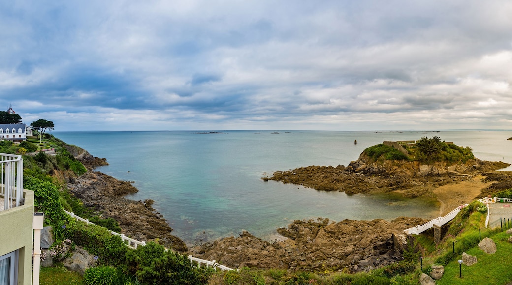 A coastal landscape with rocky outcrops, a white building, and a clear view of the sea.