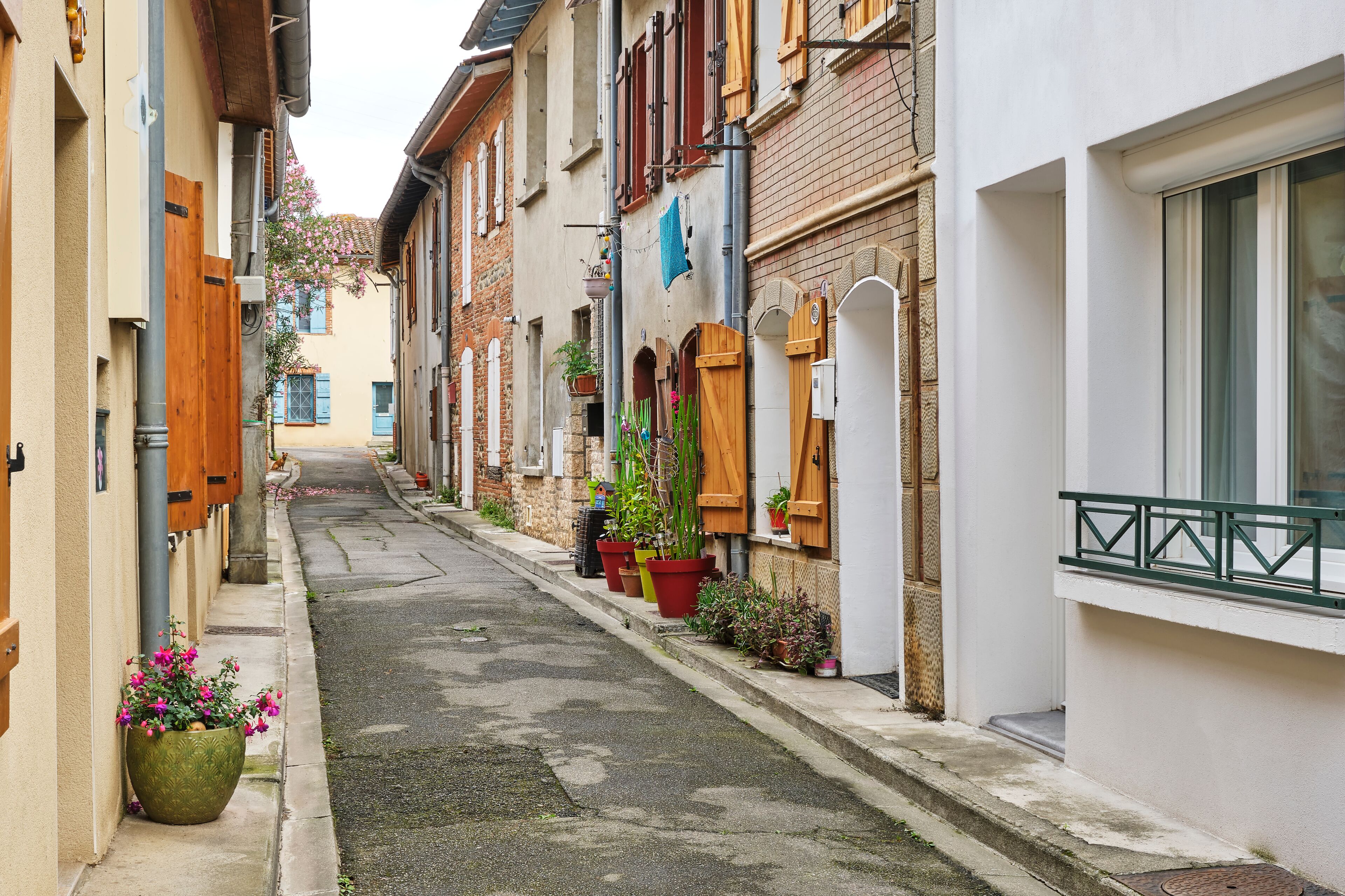 Traditional narrow street in Portet-sur-Garonne in Haute-Garonne Occitanie Southern France with brick and plastered houses with shutters and pots with plants on the street.