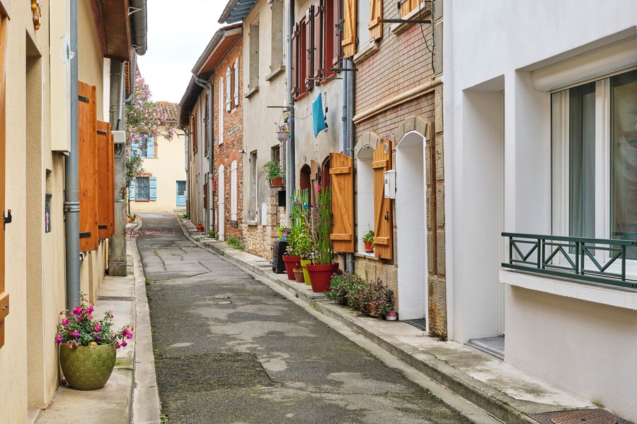 Traditional narrow street in Portet-sur-Garonne in Haute-Garonne Occitanie Southern France with brick and plastered houses with shutters and pots with plants on the street.