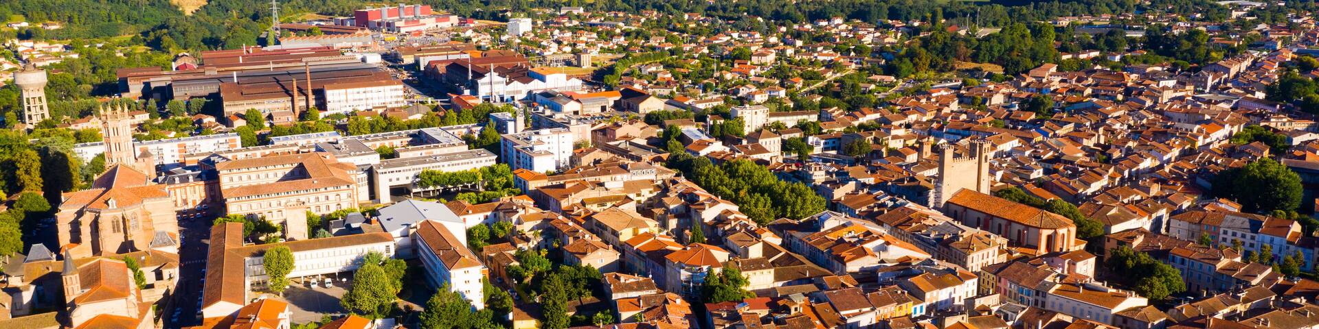 Aerial view of residential areas of Pamiers town with similar brownish roofs in green valley of Ariege River on summer day, Occitanie