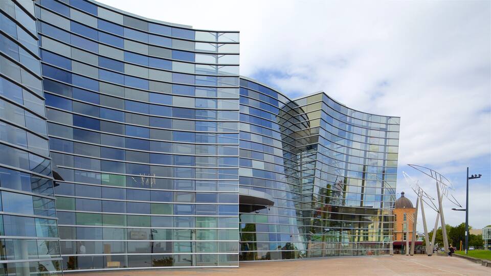 Un edificio moderno de vidrio con fachada curva y una estructura en forma de cúpula al fondo.