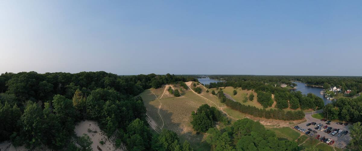 A forested landscape with a lake, a parking lot, and a few buildings.
