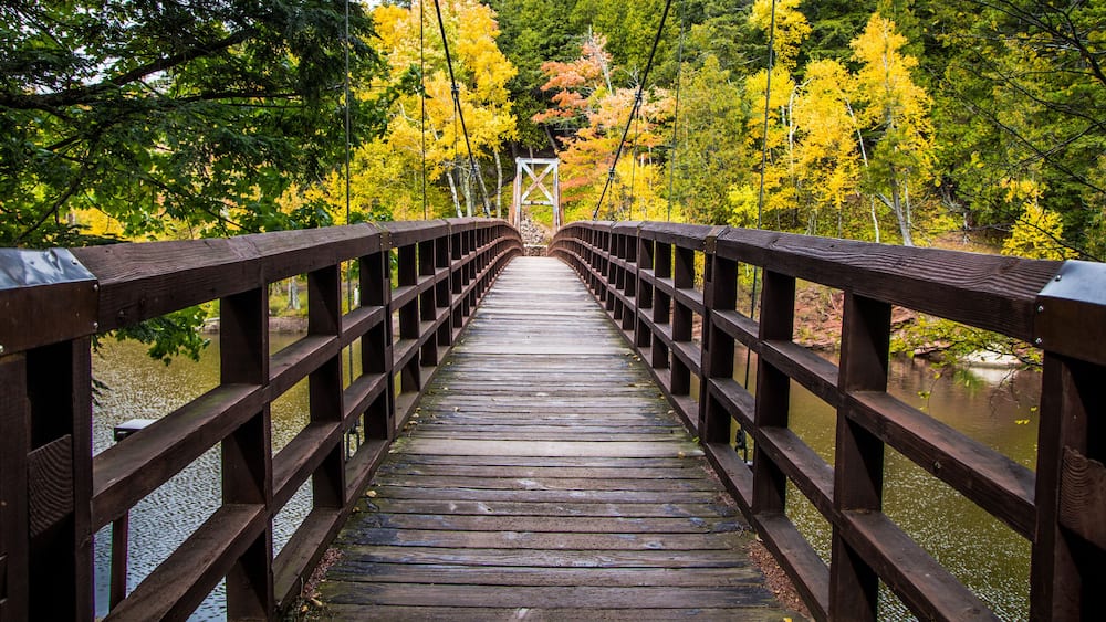 A wooden bridge over a calm river surrounded by autumn foliage.