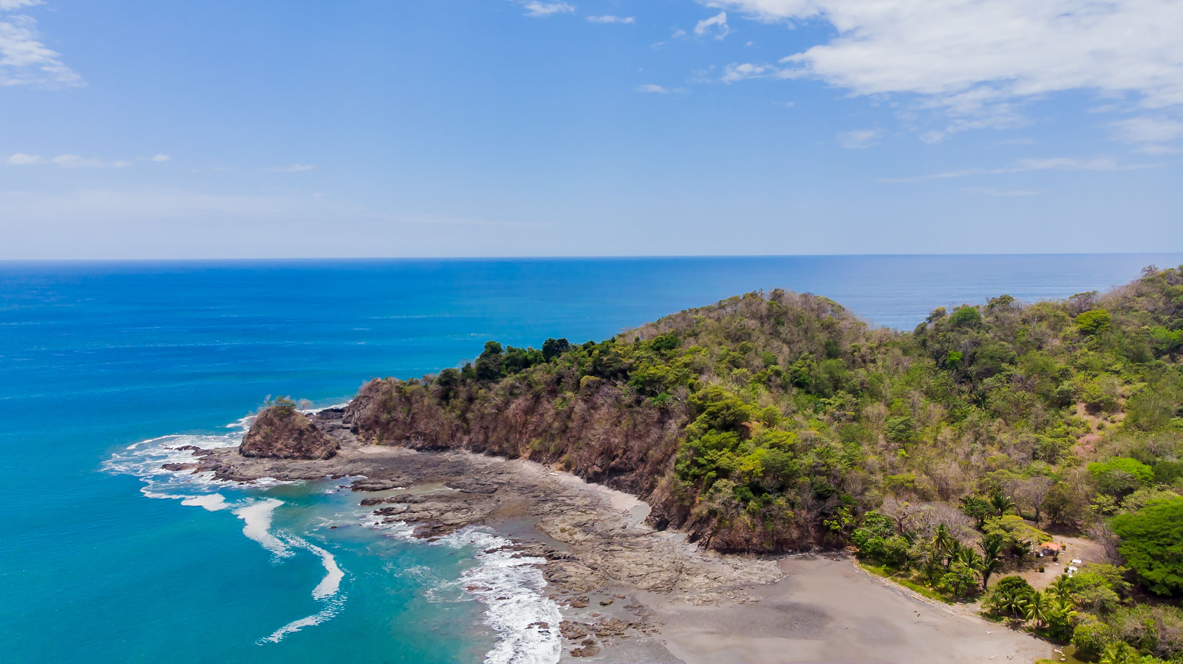 A coastal landscape with a rocky shoreline, clear blue sea, and dense green vegetation.