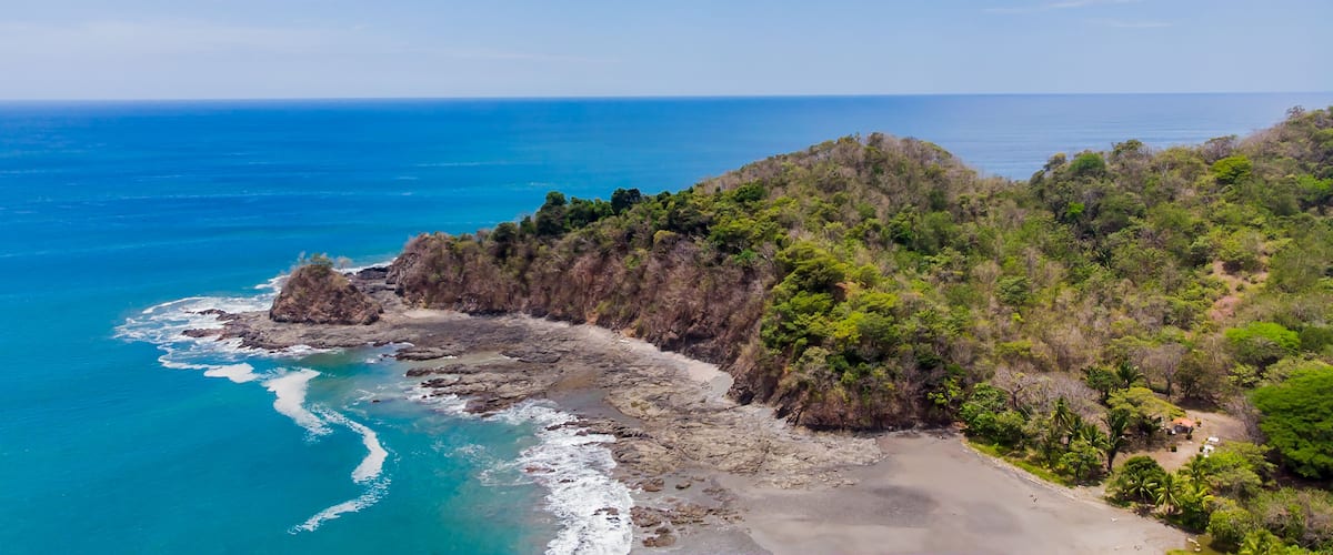 A coastal landscape with a rocky shoreline, clear blue sea, and dense green vegetation.