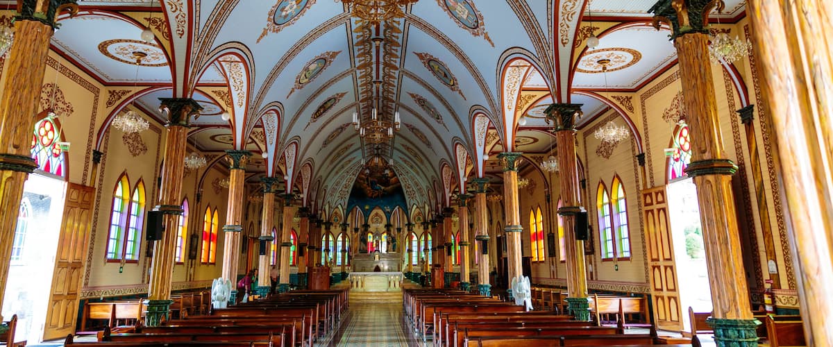 An ornate church interior with high ceilings, stained glass windows, and rows of pews.