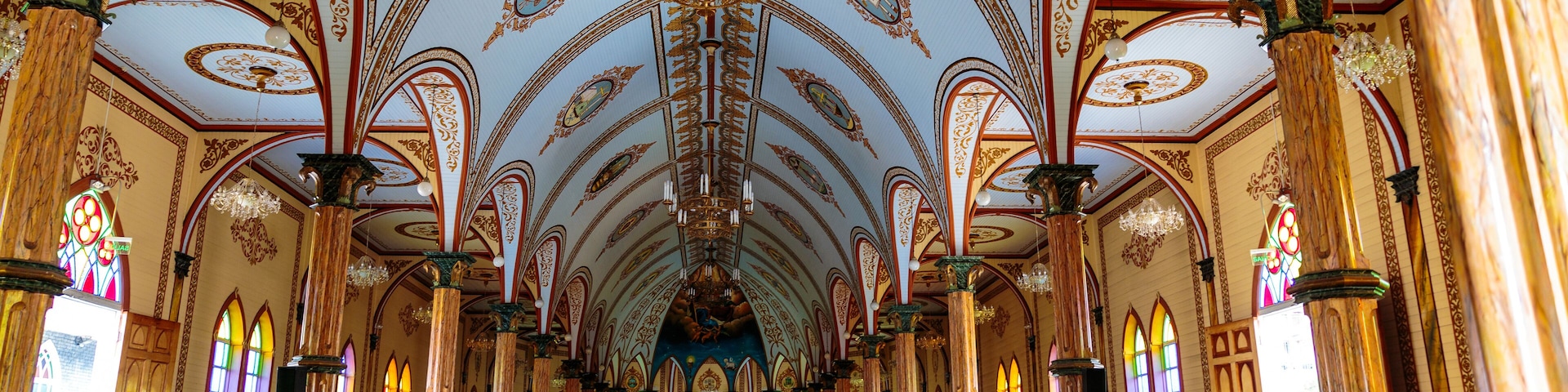 An ornate church interior with high ceilings, stained glass windows, and rows of pews.