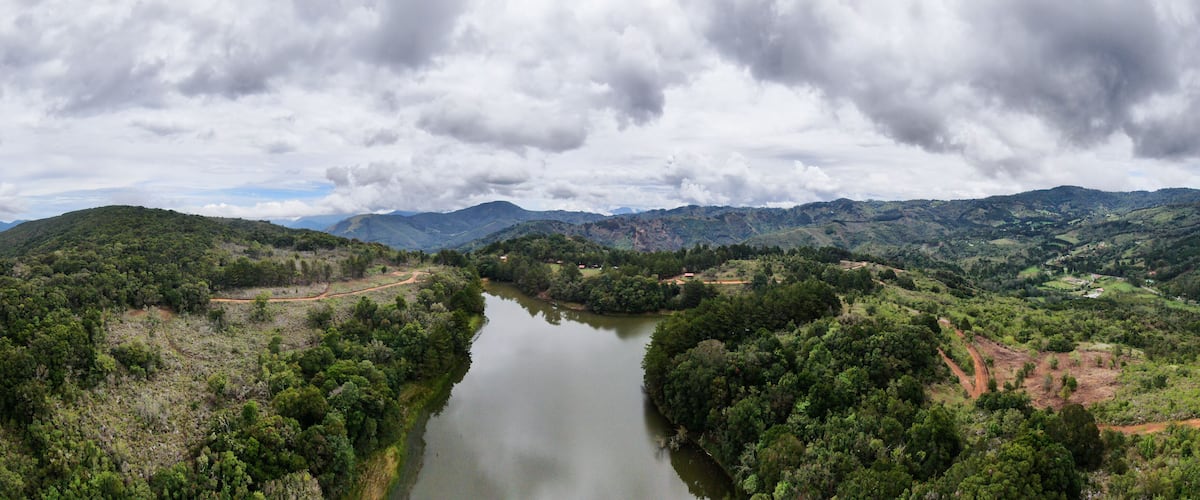 A river winding through a mountainous landscape with dense forests and a cloudy sky.