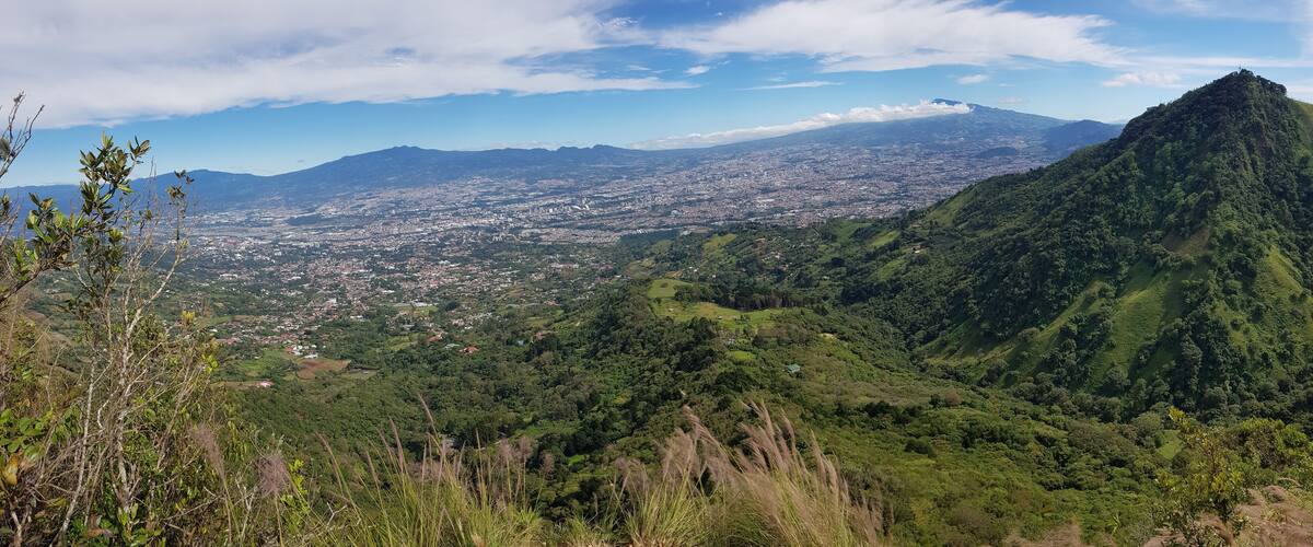 A mountainous landscape with a city in the valley, lush greenery, and a clear sky.