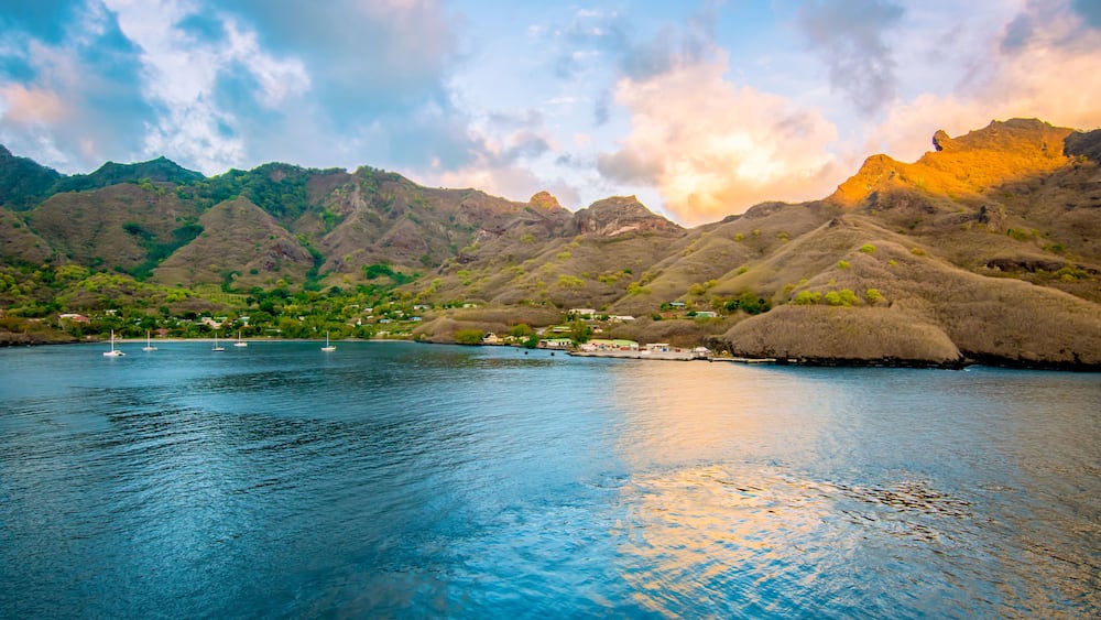 A coastal landscape with mountains, a calm sea, and a few boats.