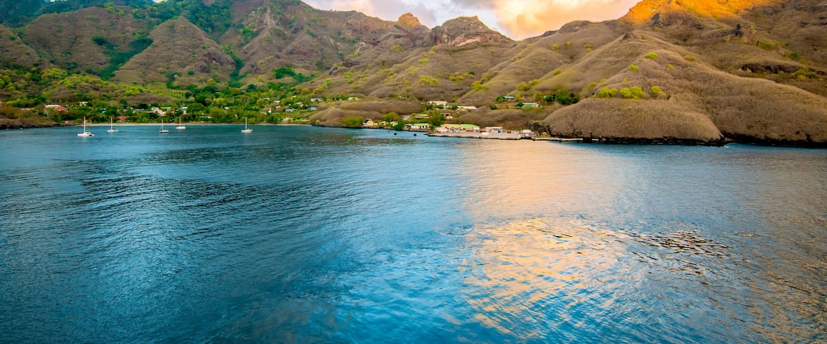 A coastal landscape with mountains, a calm sea, and a few boats.