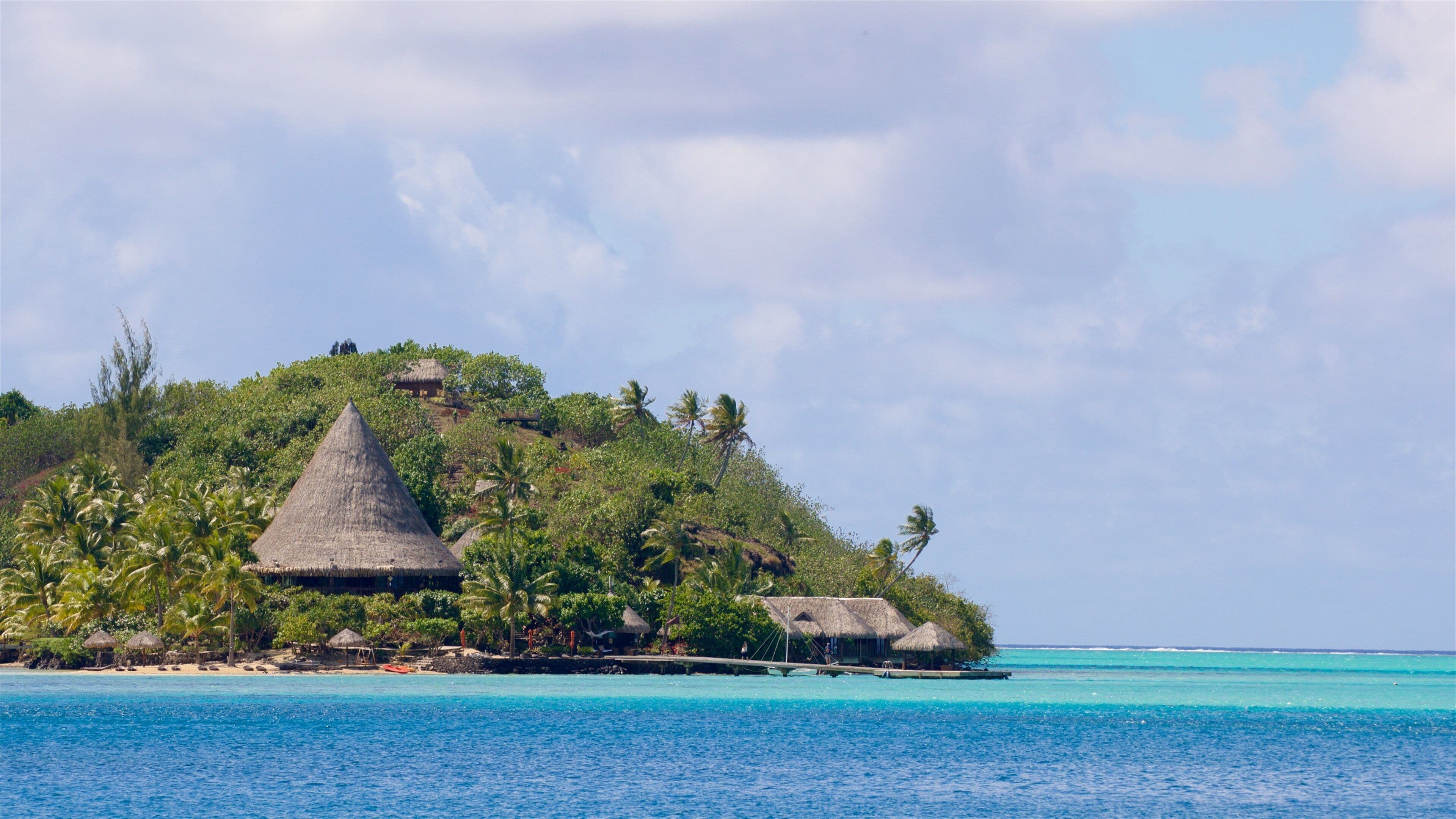 A tropical island with thatched-roof huts surrounded by palm trees and clear blue waters.