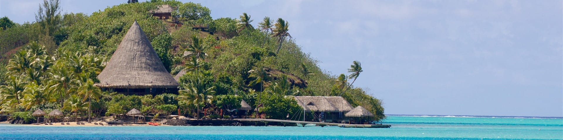 Una isla tropical con chozas de techo de paja rodeadas de palmeras y aguas azul turquesa.