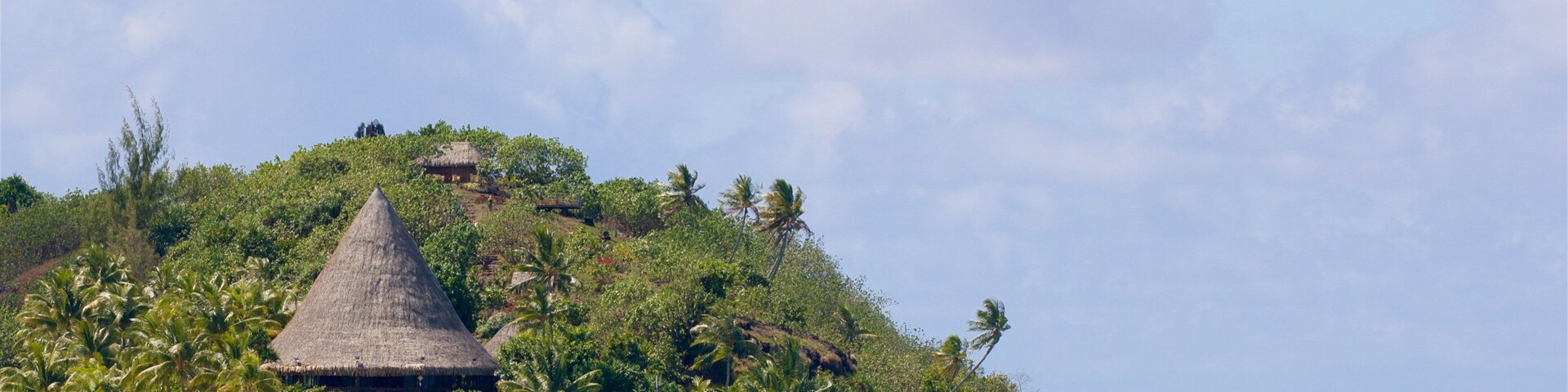Uma ilha tropical com palafitas de telhado de palha, rodeada por palmeiras e águas cristalinas.