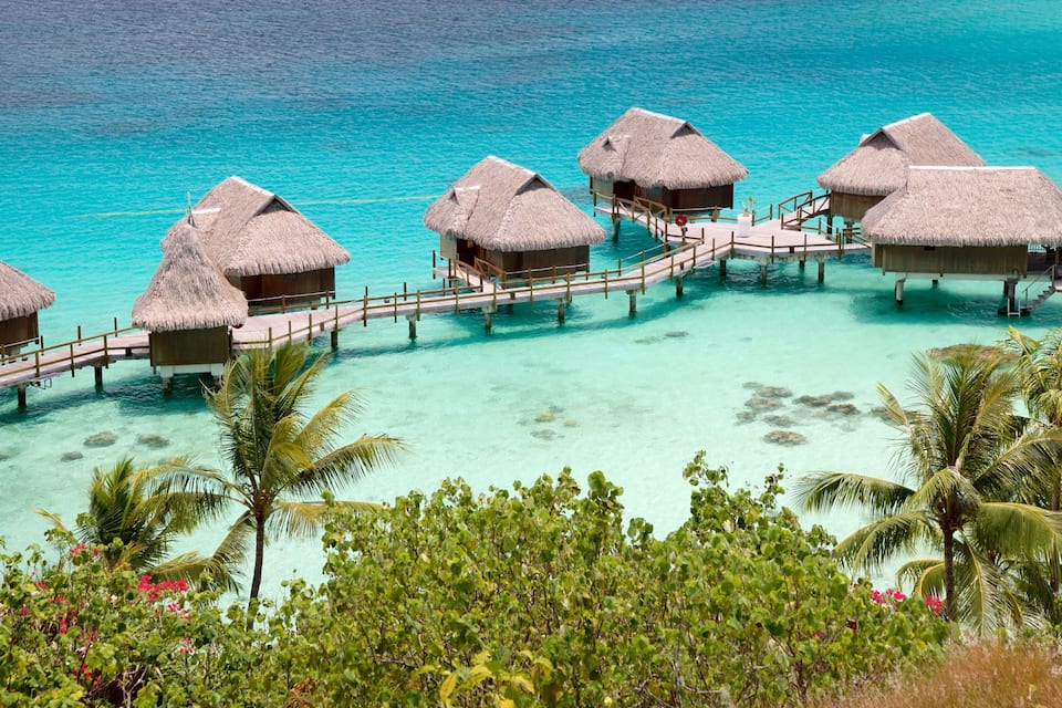 Overwater bungalows with thatched roofs connected by wooden walkways over turquoise water.