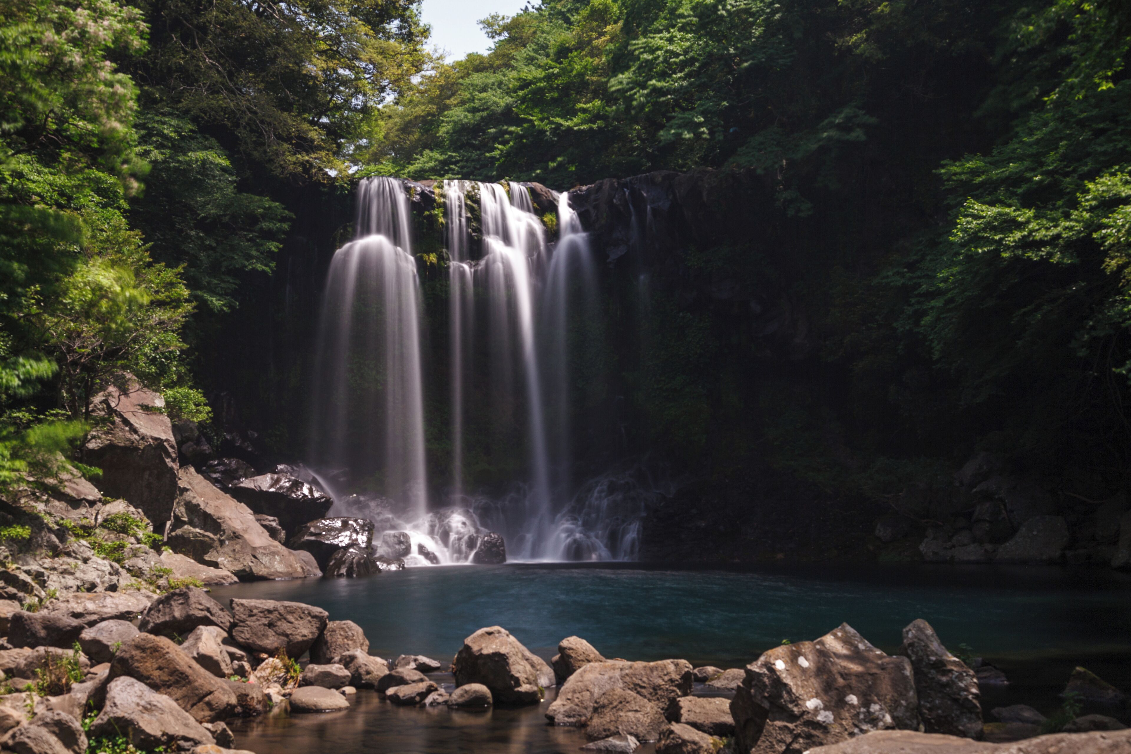 A waterfall cascading into a clear pool surrounded by rocks and lush greenery.