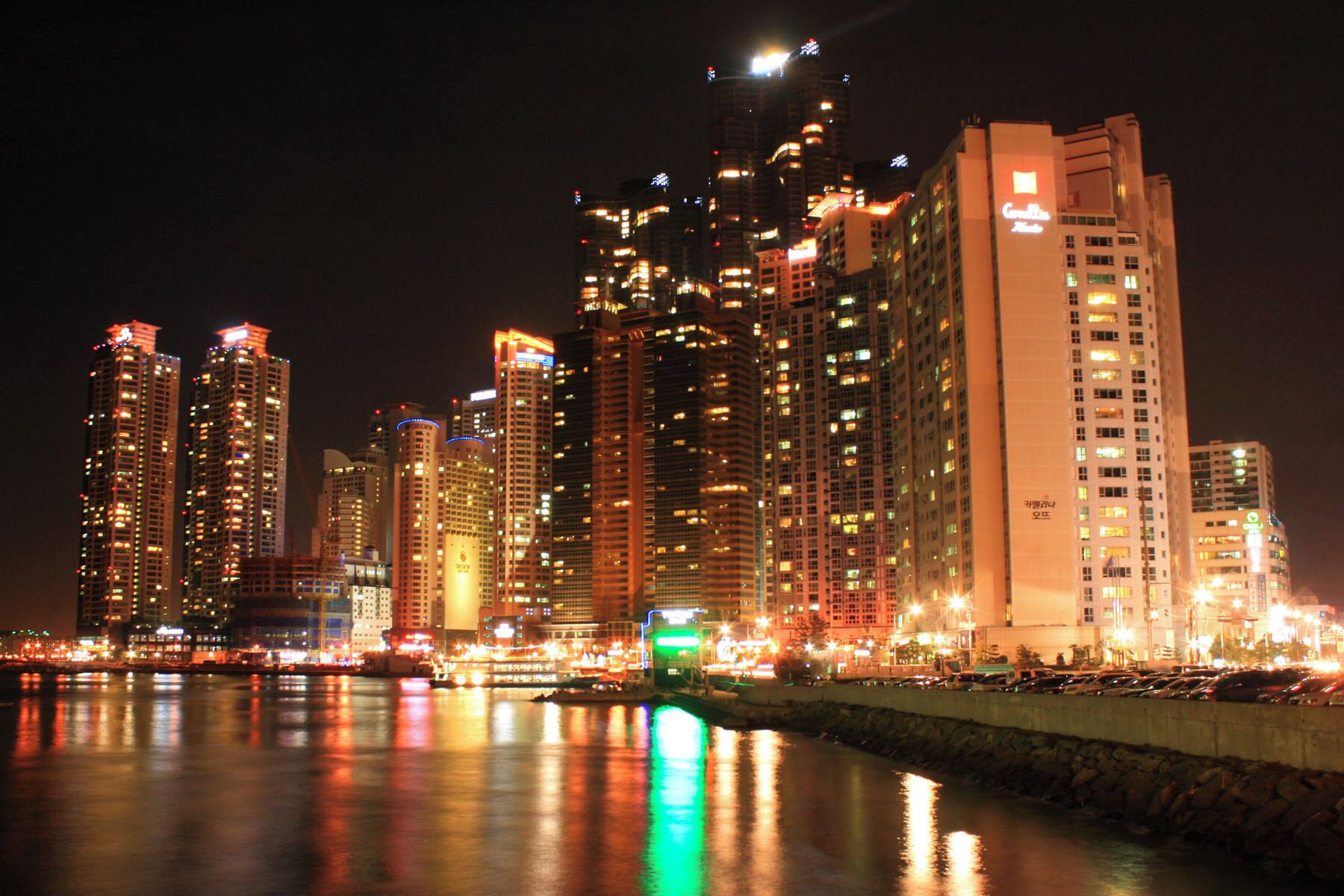 A city skyline at night with illuminated buildings reflecting on the water.