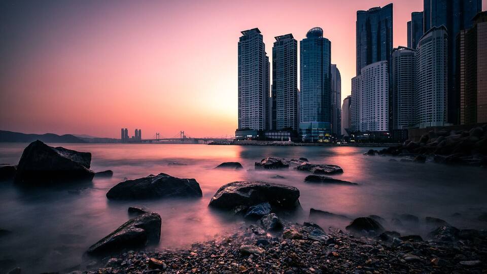 Un paisaje urbano al atardecer con un río en primer plano y rascacielos al fondo.