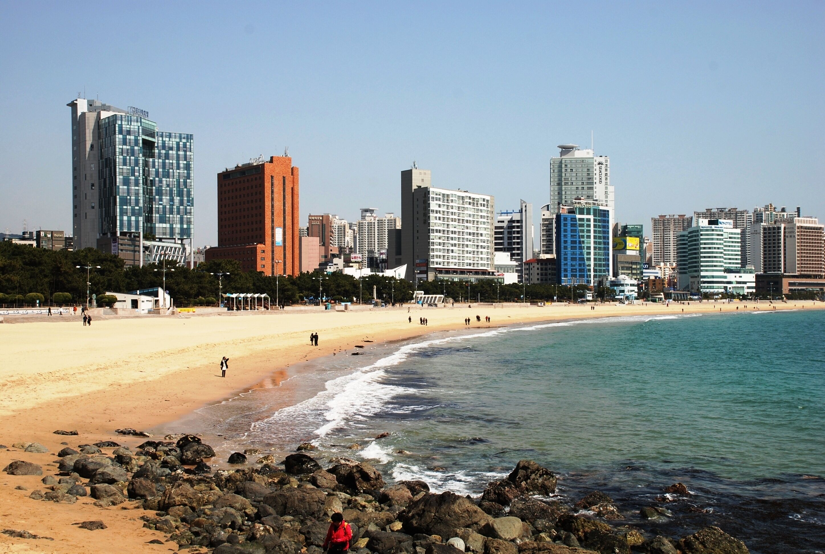 Ein Strand mit felsigem Ufer, einem Sandstrand und einer Stadtlandschaft mit hohen Gebäuden im Hintergrund.