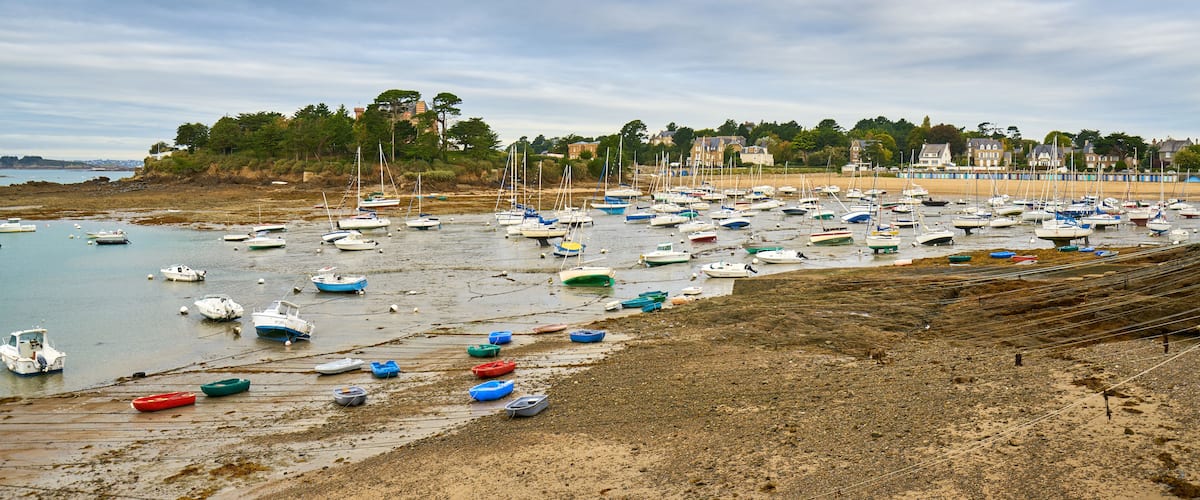 A beach with numerous small boats, a sandy shore, and a line of buildings in the background.