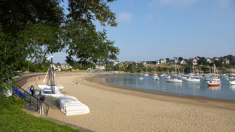 Une plage avec des bateaux, un rivage sablonneux et des maisons en arrière-plan.
