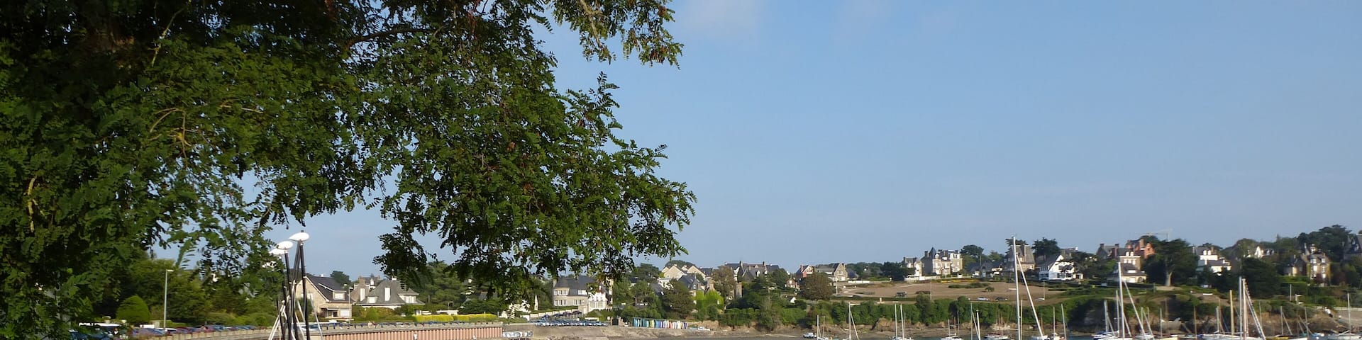 A beach with boats, a sandy shore, and houses in the background.