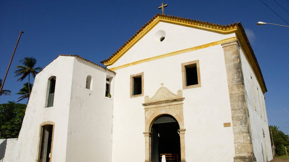 A white church with a cross on top, a bell tower, and a large arched entrance.