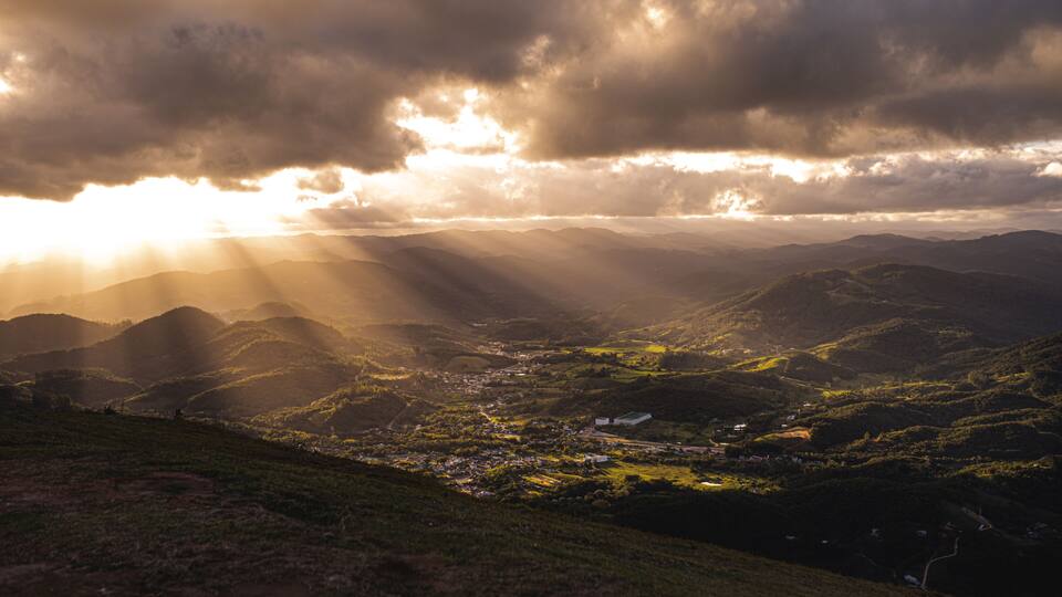 A valley with mountains, a small town, and sunlight filtering through clouds.