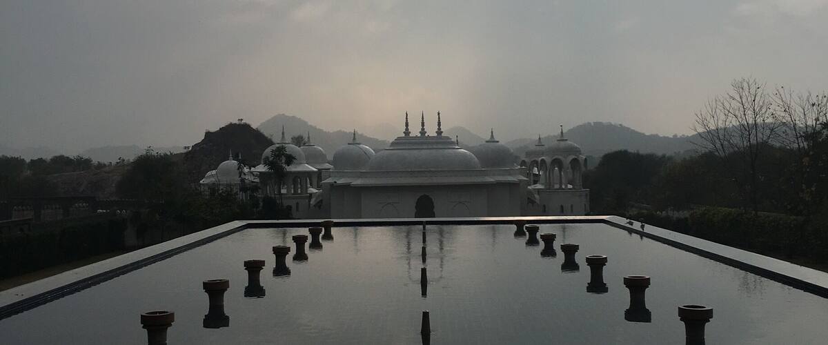 A reflective pool with a symmetrical arrangement of pillars leading to a temple with multiple domes.