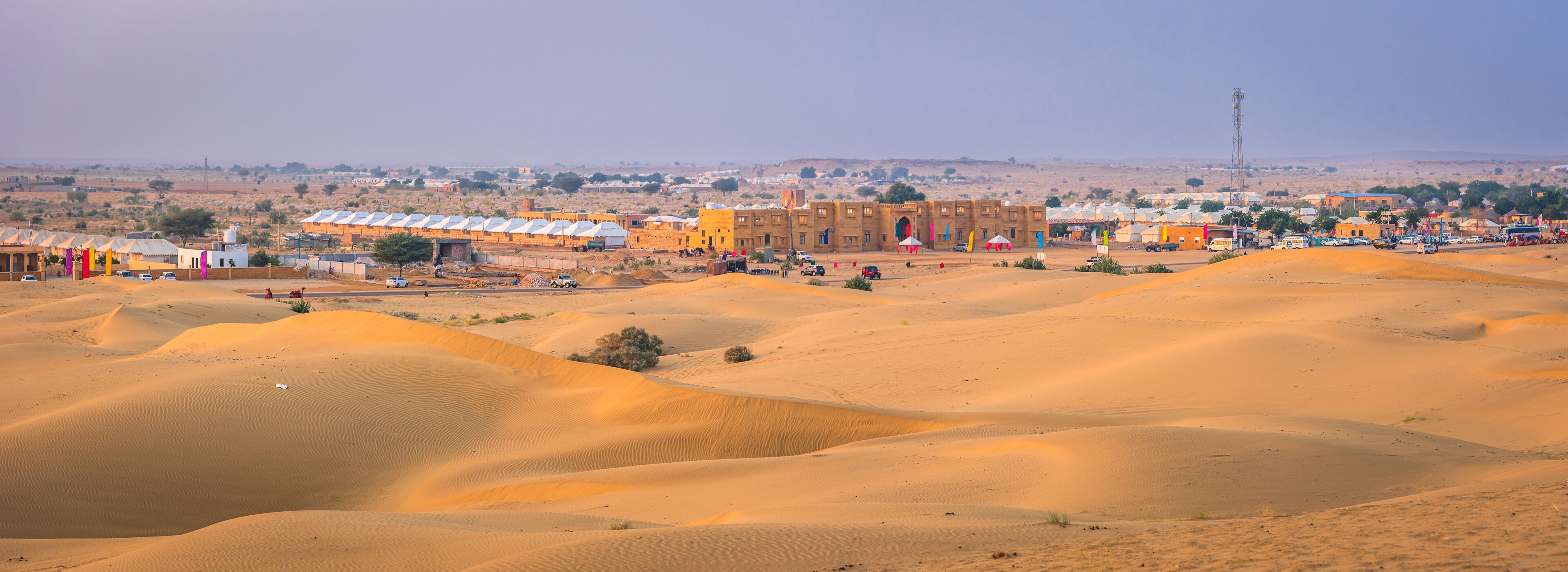 A desert landscape with sand dunes, a town with buildings, and a distant tower.