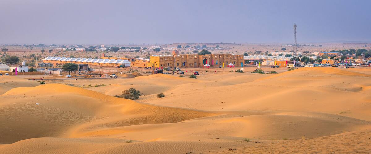 A desert landscape with sand dunes, a town with buildings, and a distant tower.