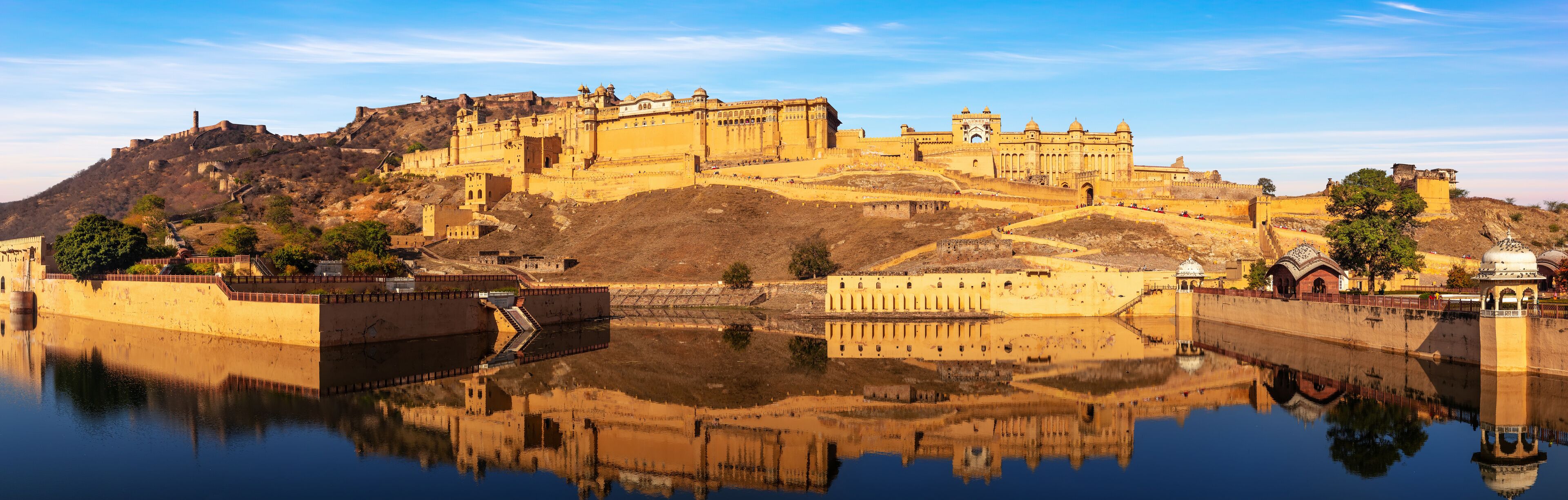 Un complejo histórico de fortaleza y palacio con una extensa masa de agua en primer plano que refleja las estructuras.
